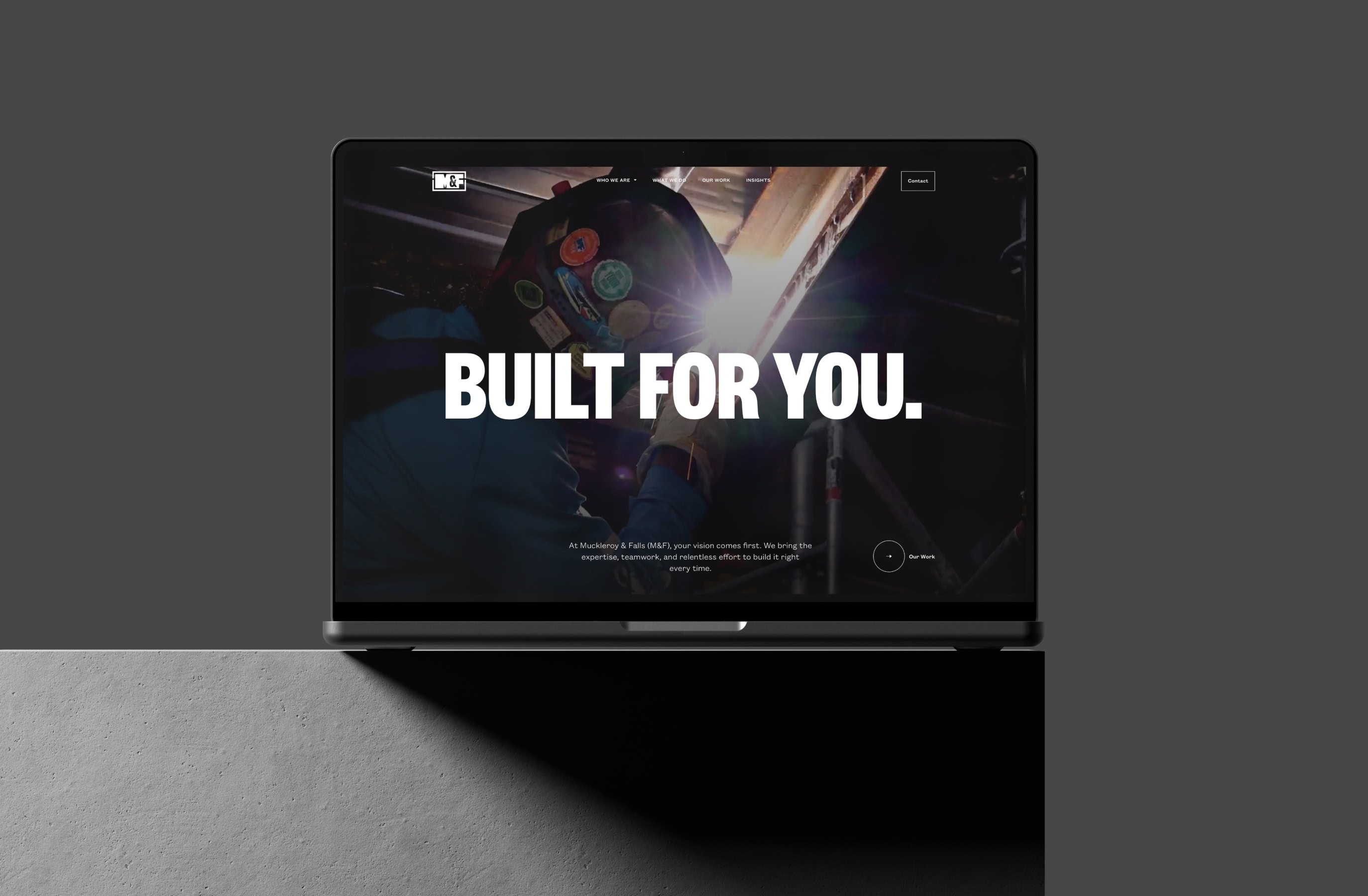 Laptop screen displaying a construction worker welding, wearing a helmet. The bold text 