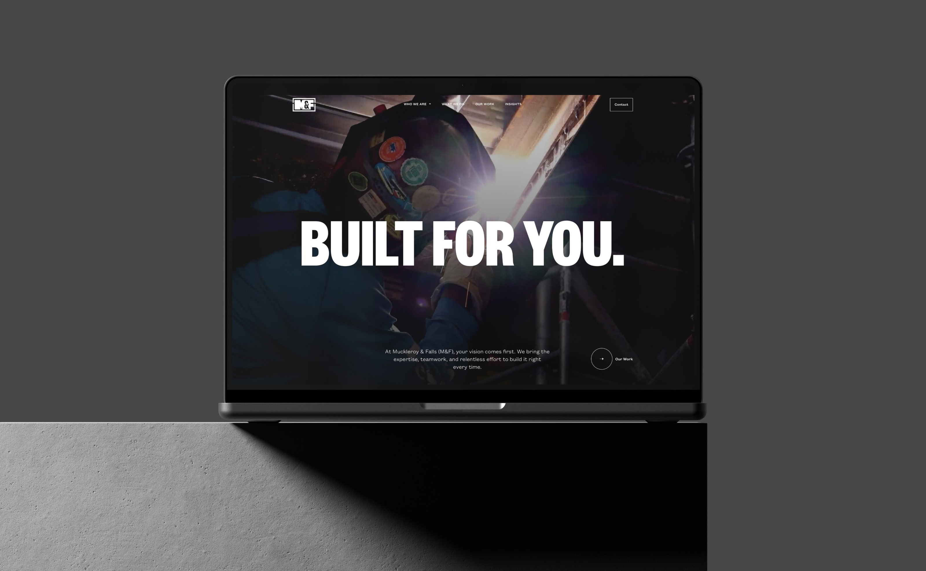Laptop screen displaying a construction worker welding, wearing a helmet. The bold text 