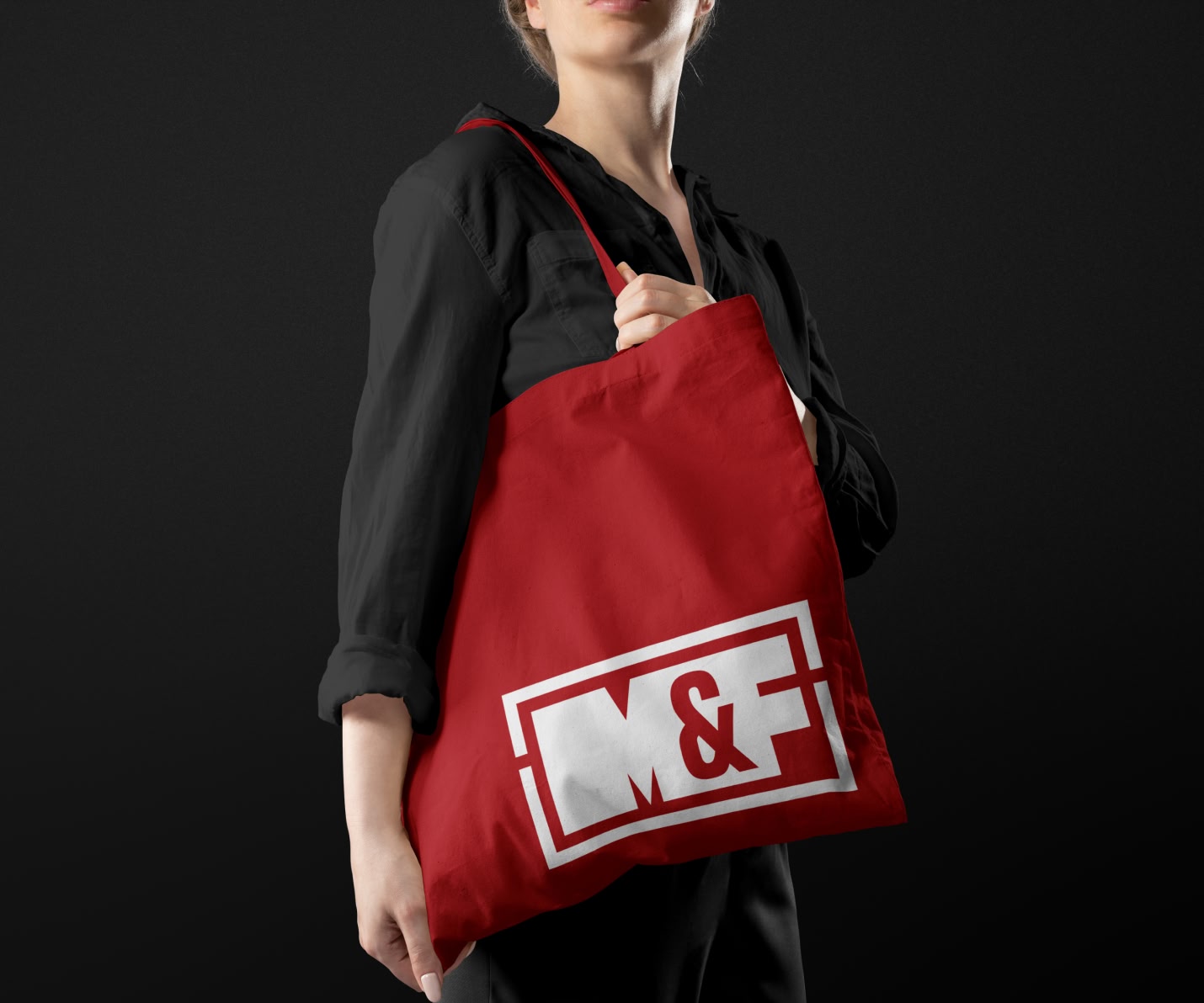 Woman holding a red tote bag with the Muckleroy & Falls logo mark on the bag