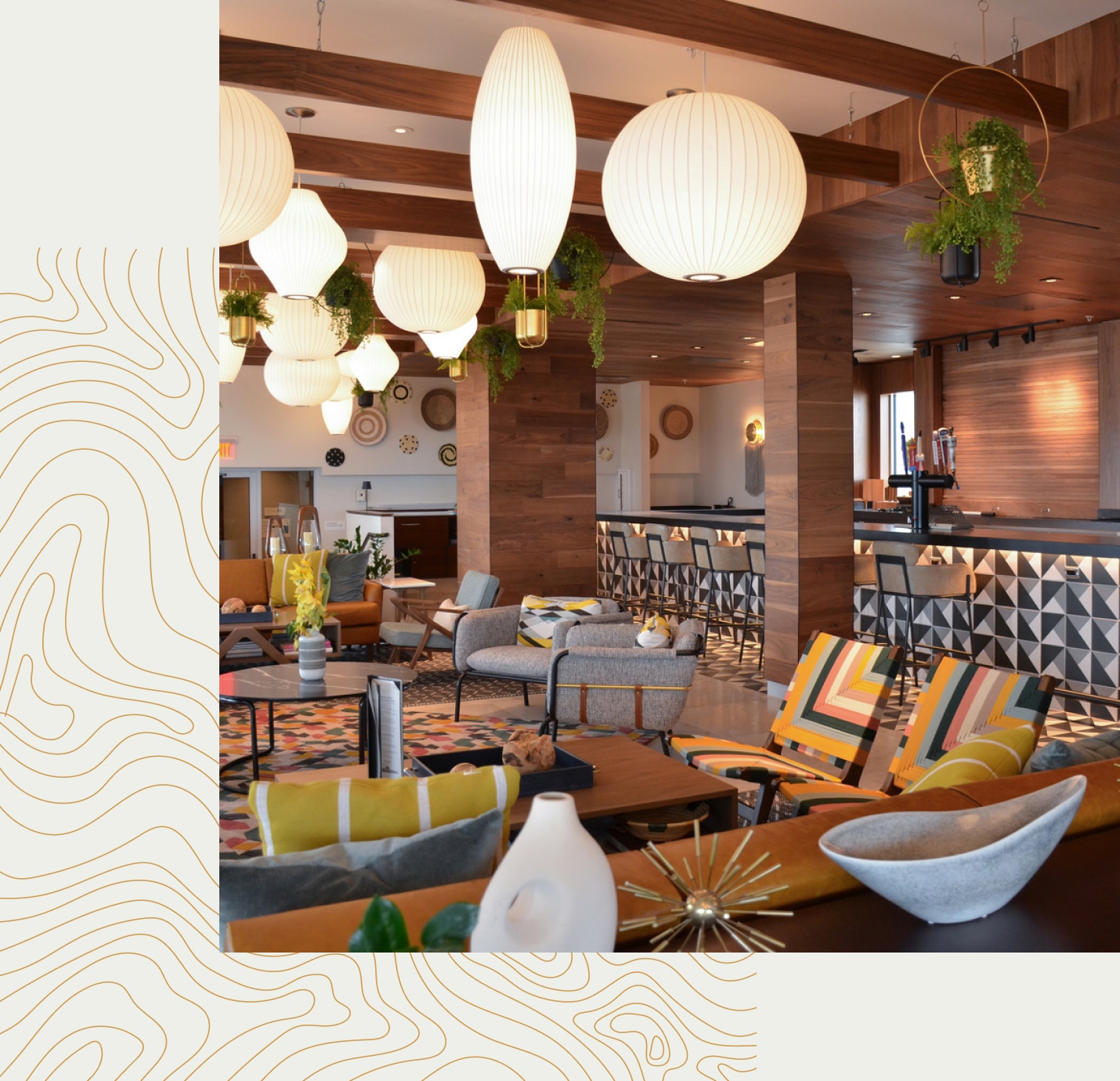 Modern lounge with mid-century decor, featuring patterned chairs, geometric bar, and large hanging lights. Warm, inviting atmosphere with wood accents.