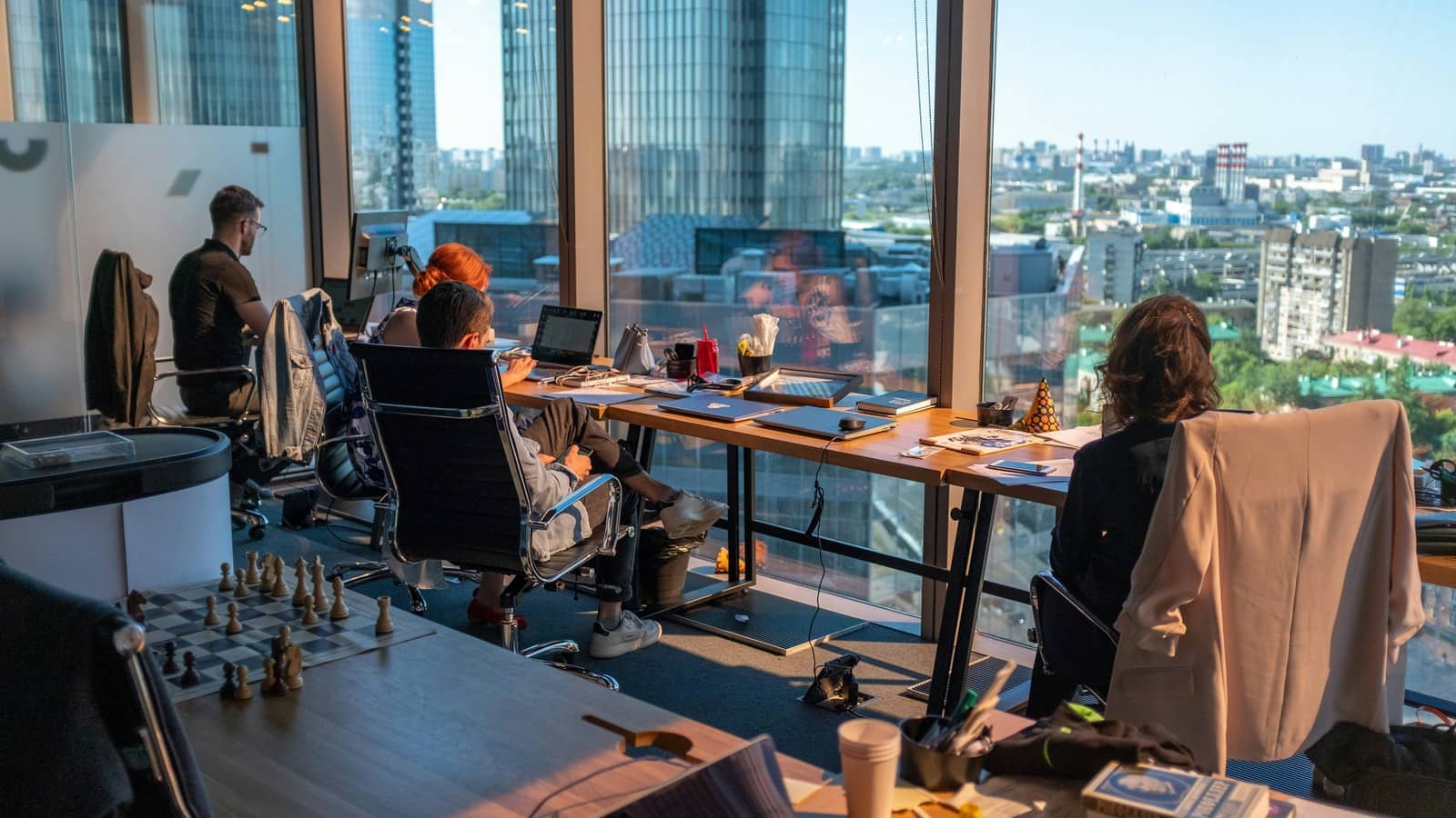 AEC firm team members working at desks in a contemporary high-rise office space with panoramic city views, representing modern architecture and engineering firm culture.