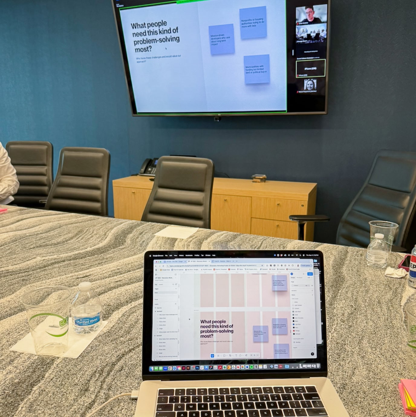 Meeting room with a large screen displaying a presentation on problem-solving. A laptop on the table mirrors the screen. The mood is professional.