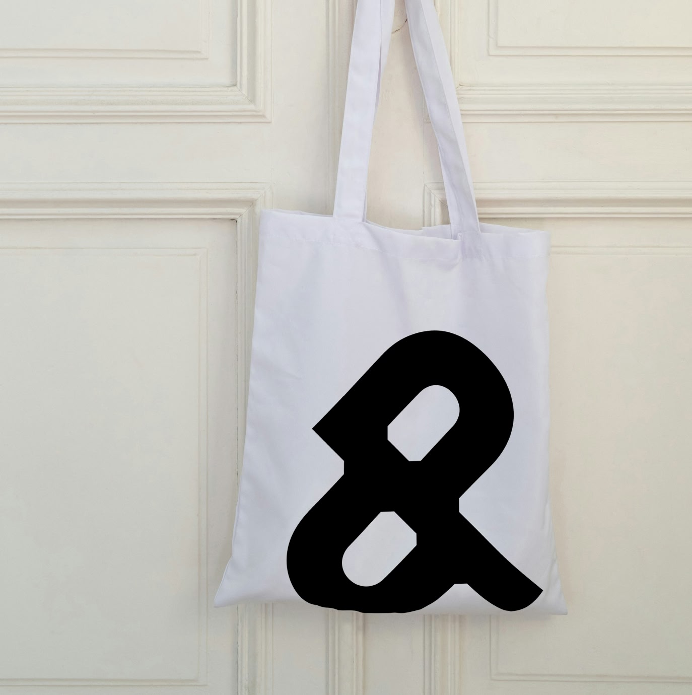 white tote bag hanging on a door with black logo mark on it